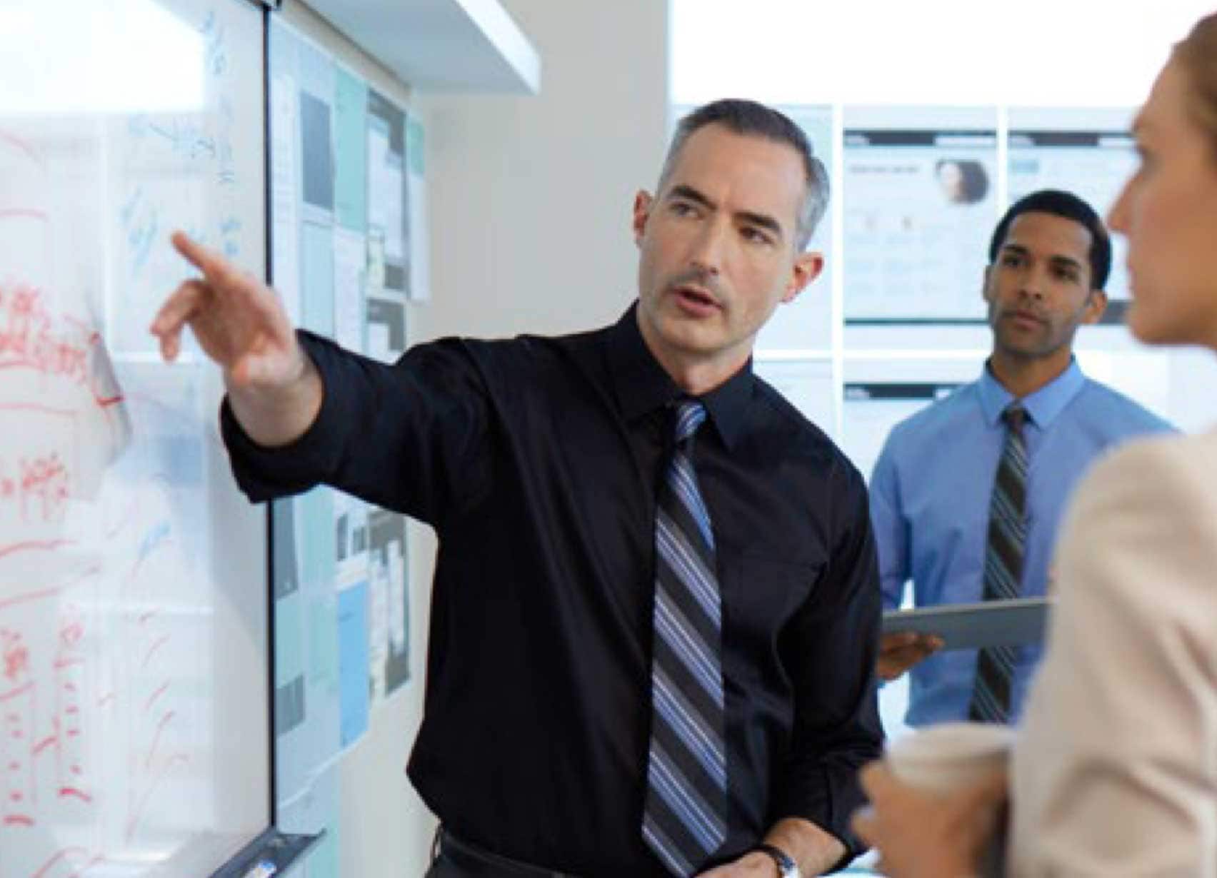 Man pointing at whiteboard talking with co-workers